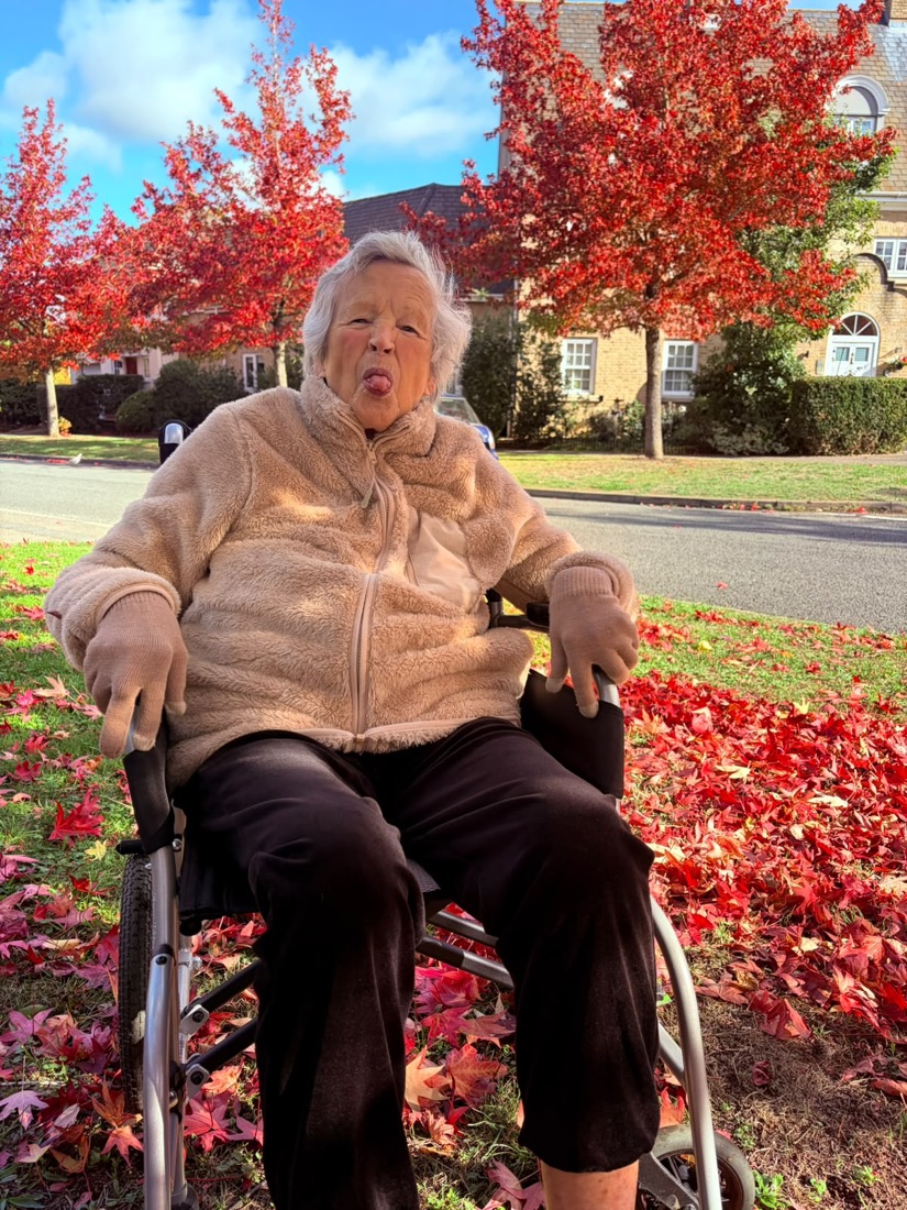 Josie in her wheelchair among red autumn leaves, cheekily sticking her tongue out at the camera
